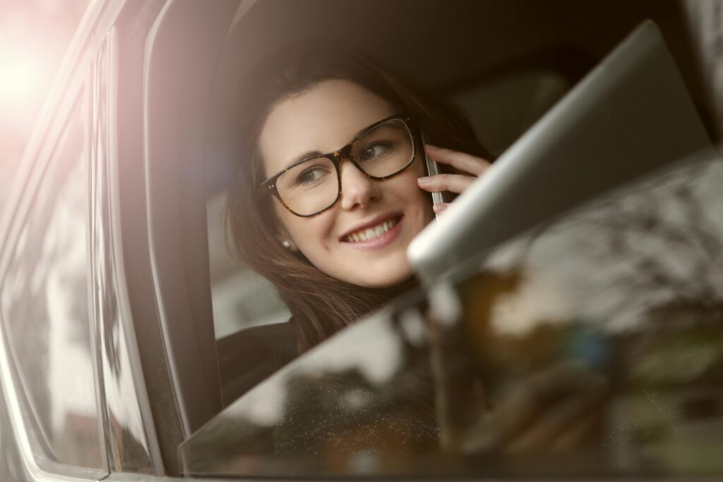 Female in glasses with tablet talking on smartphone while sitting in car with opened window